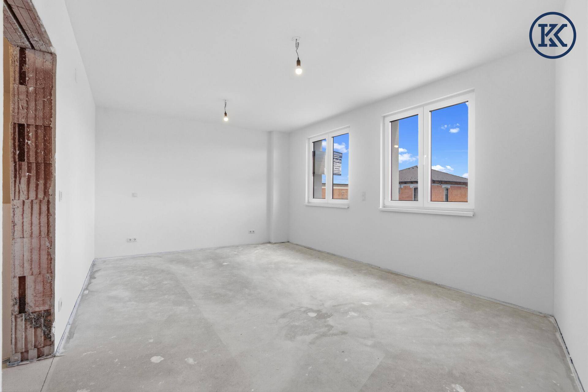 Helles Schlafzimmer im Rohbau mit zwei Fenstern und Blick auf die Umgebung, viel Tageslicht.