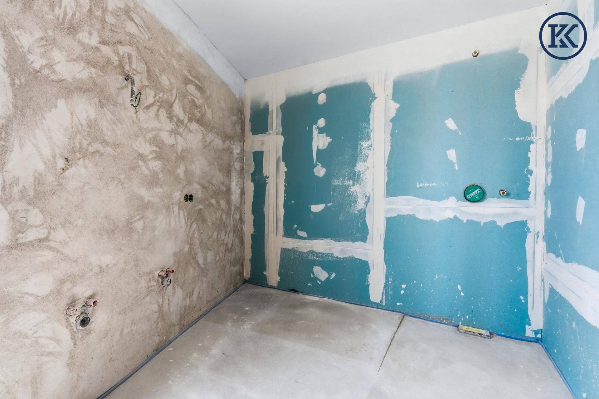 Unfertiges Badezimmer mit blauen Trockenbauwänden und vorbereiteten Anschlüssen für Sanitär.
