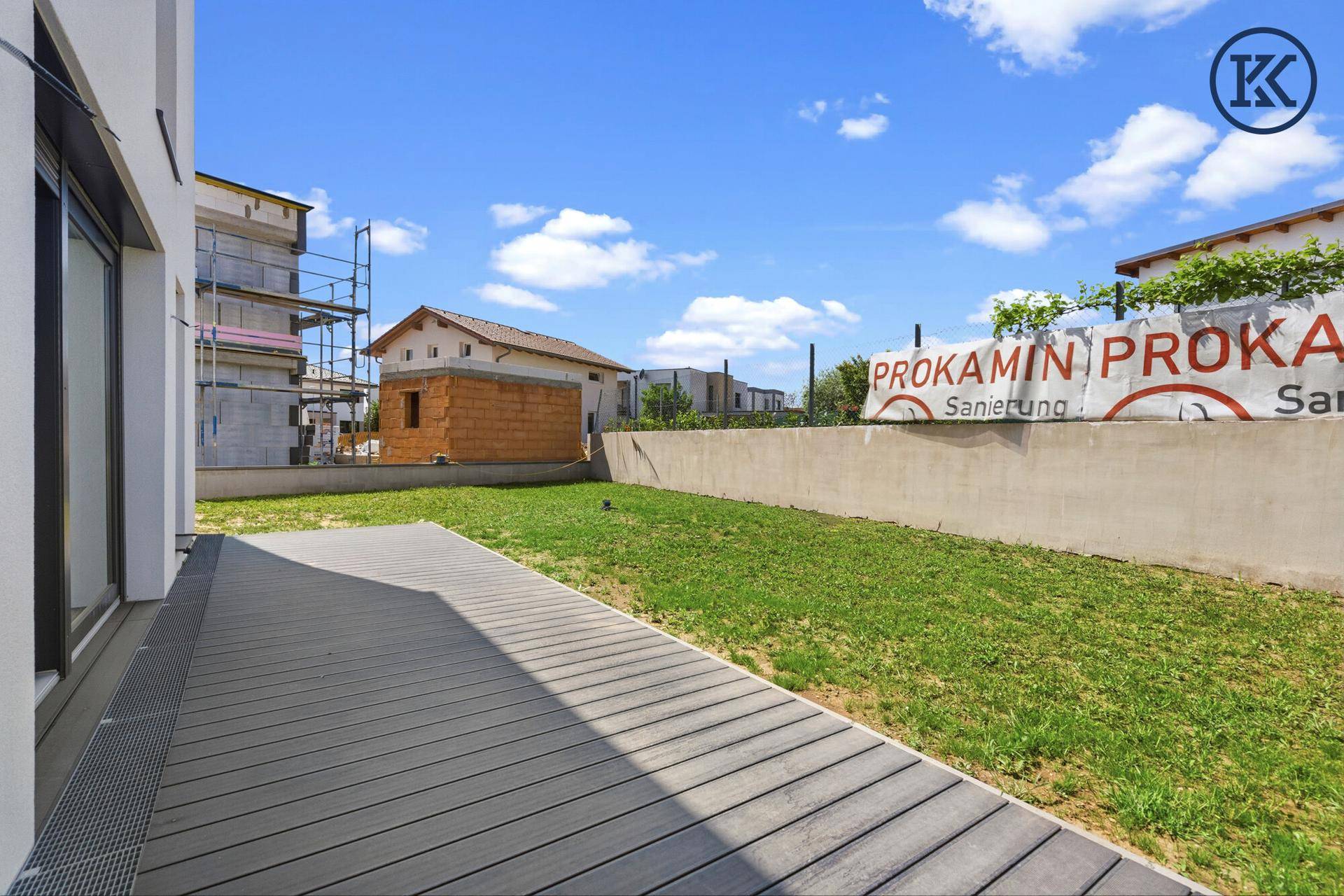 Moderne Terrasse mit Holzbelag und angrenzender Rasenfläche, umgeben von Baustellenaktivitäten.