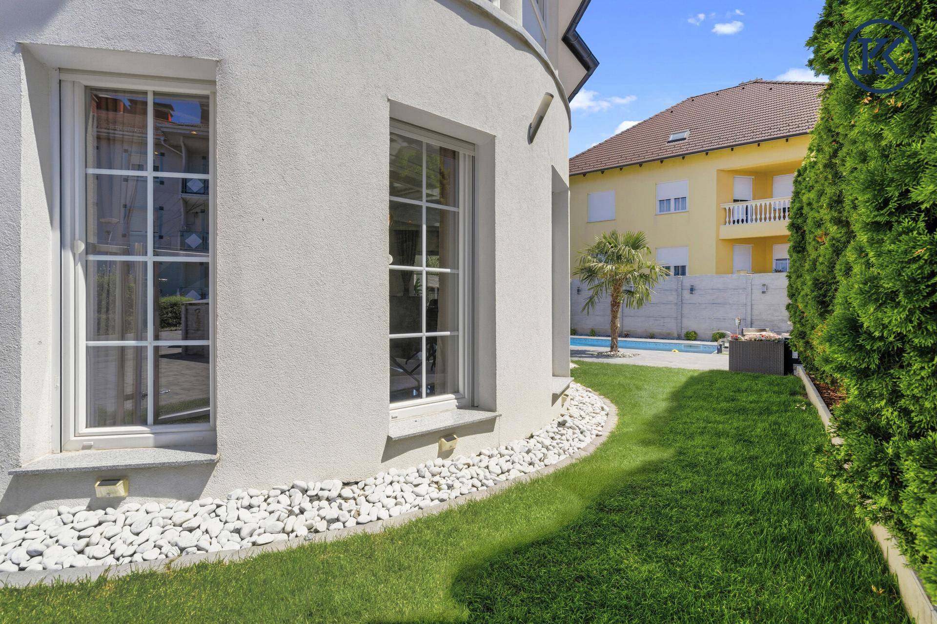 Gepflegter Gartenbereich entlang der Hausfassade mit Ziersteinen und grüner Hecke.