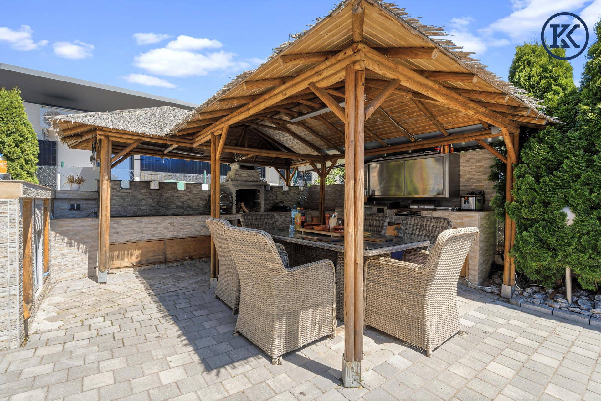 Gemütlicher Essbereich im Freien unter einem Strohdach-Pavillon mit Grillstation.