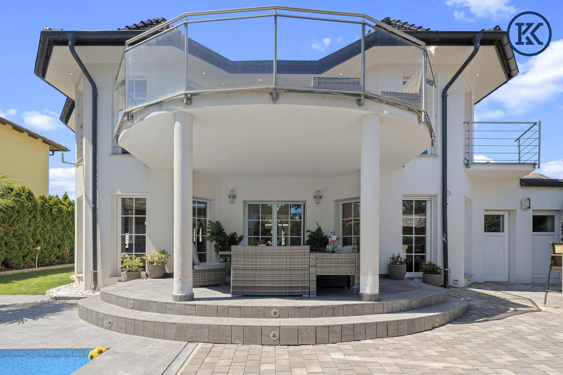 Rückseite der Villa mit großer überdachter Terrasse und einem Balkon im Obergeschoss.