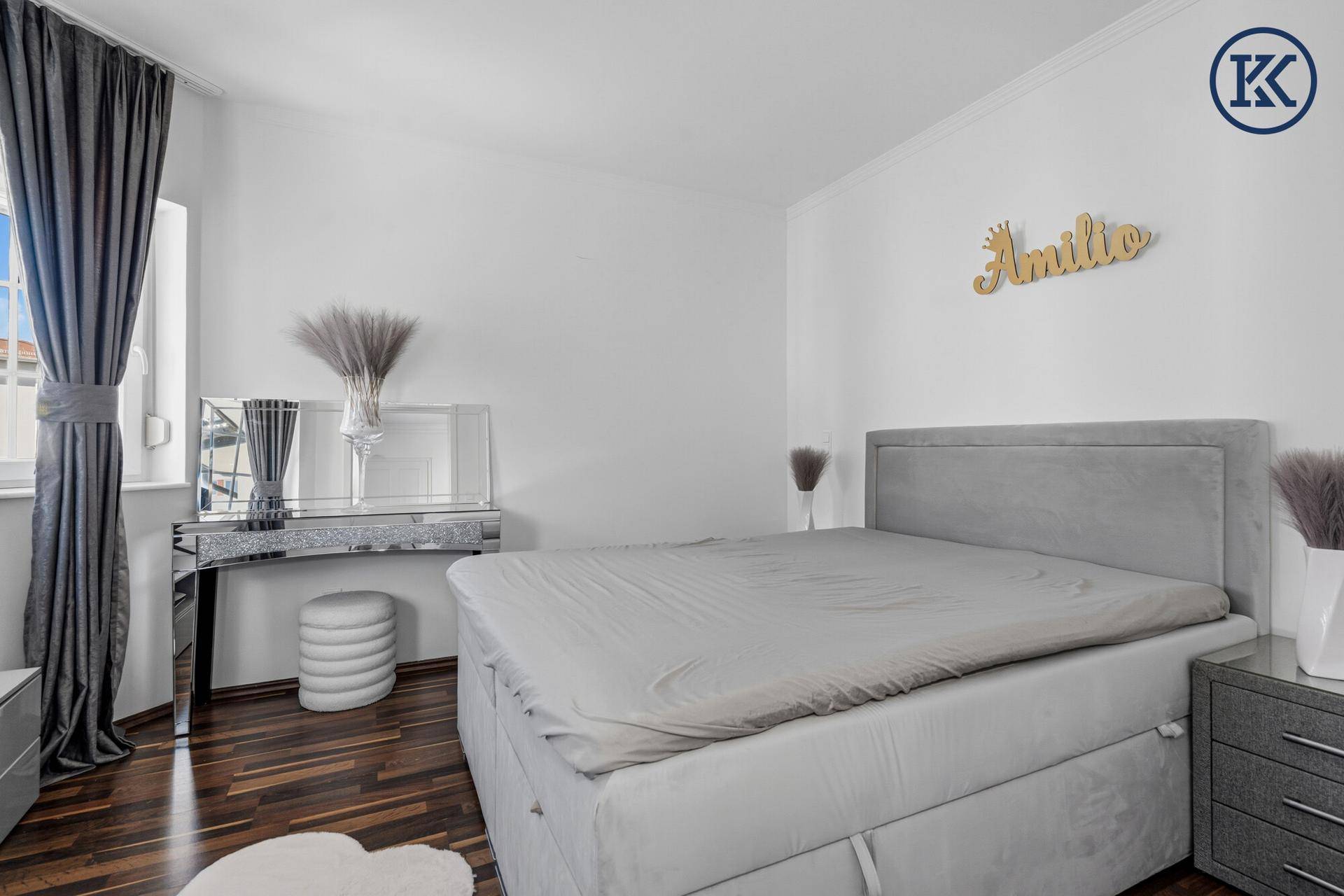 Helles Schlafzimmer mit modernem Boxspringbett, dunklem Holzboden und stilvoller Dekoration.
