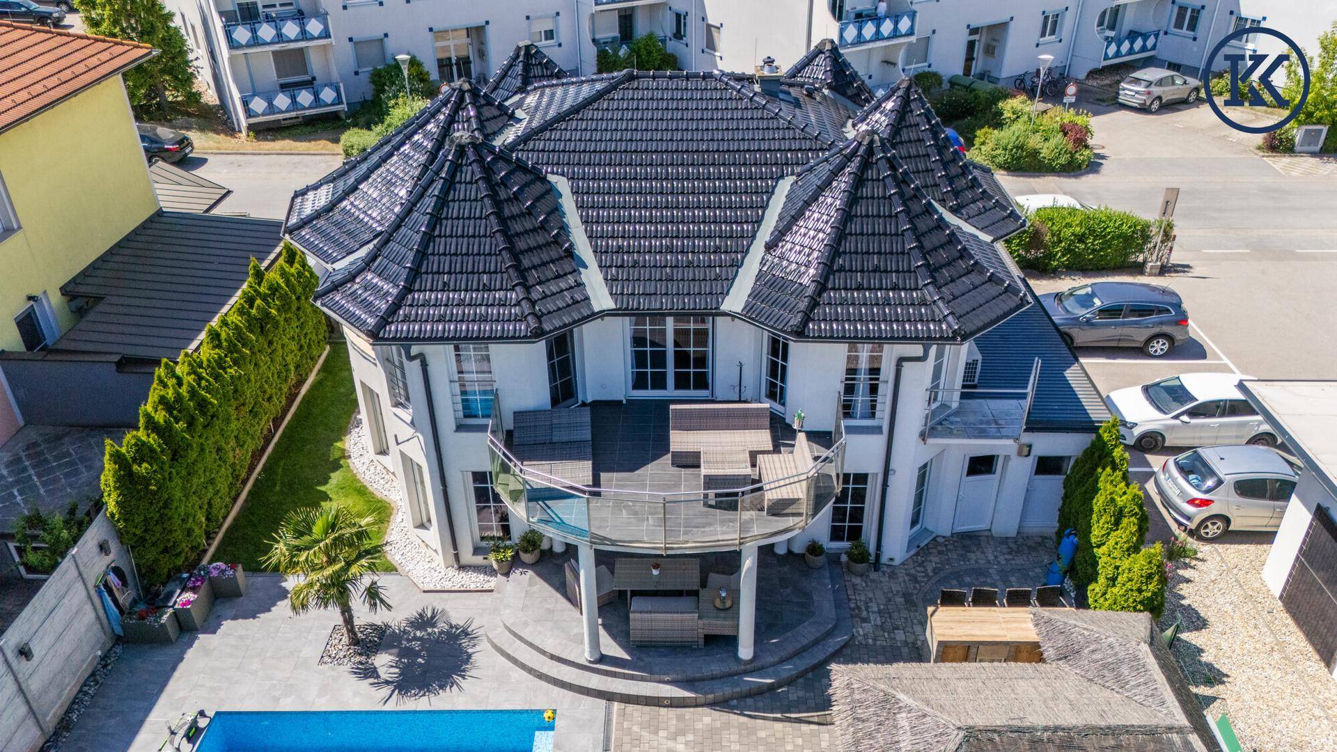 Frontansicht des Hauses von oben mit großzügiger Terrasse, Pool und gepflegter Außenanlage.