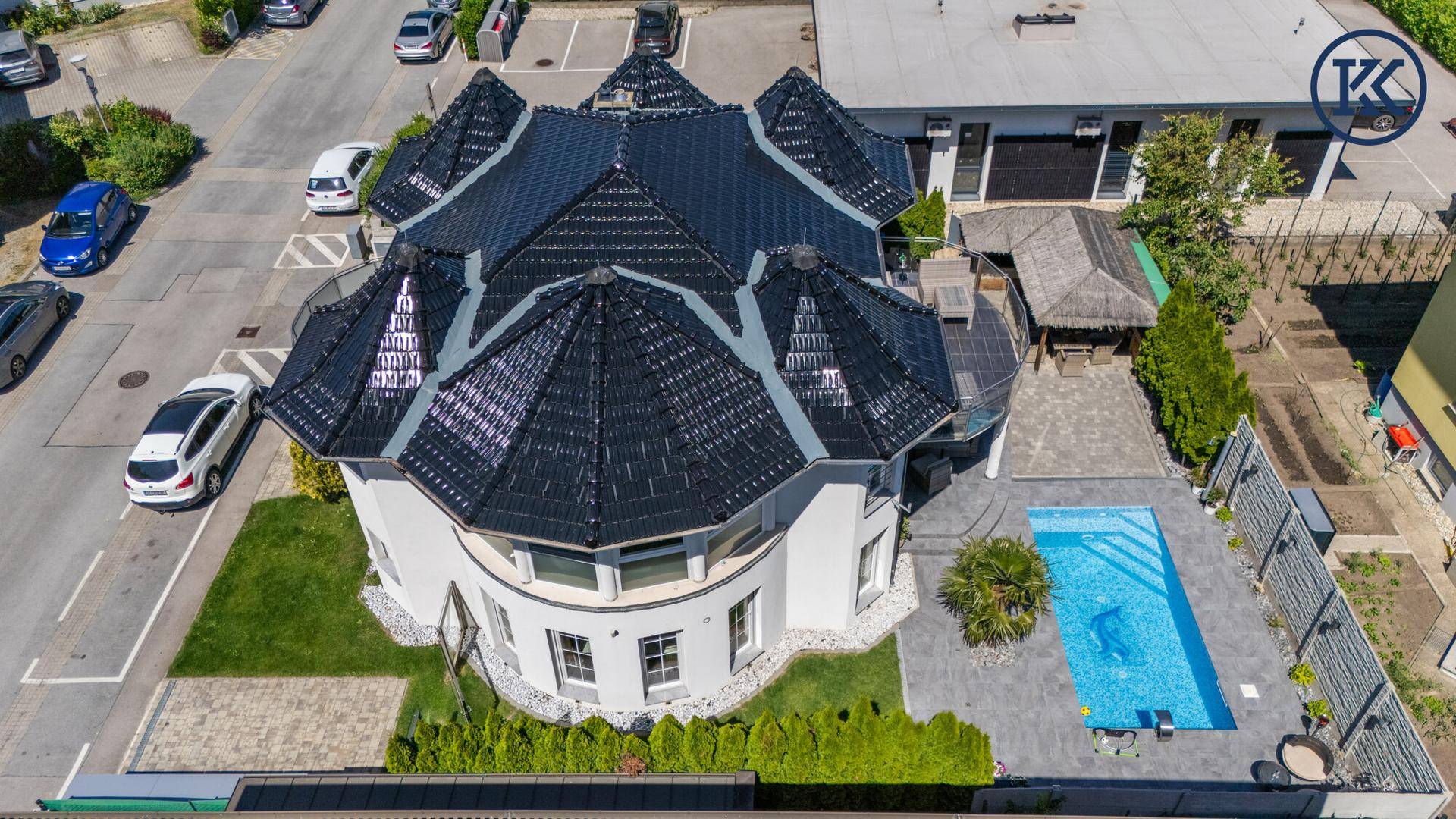 Luftaufnahme des Hauses mit Pool, Terrasse und umliegender Wohnbebauung unter blauem Himmel.