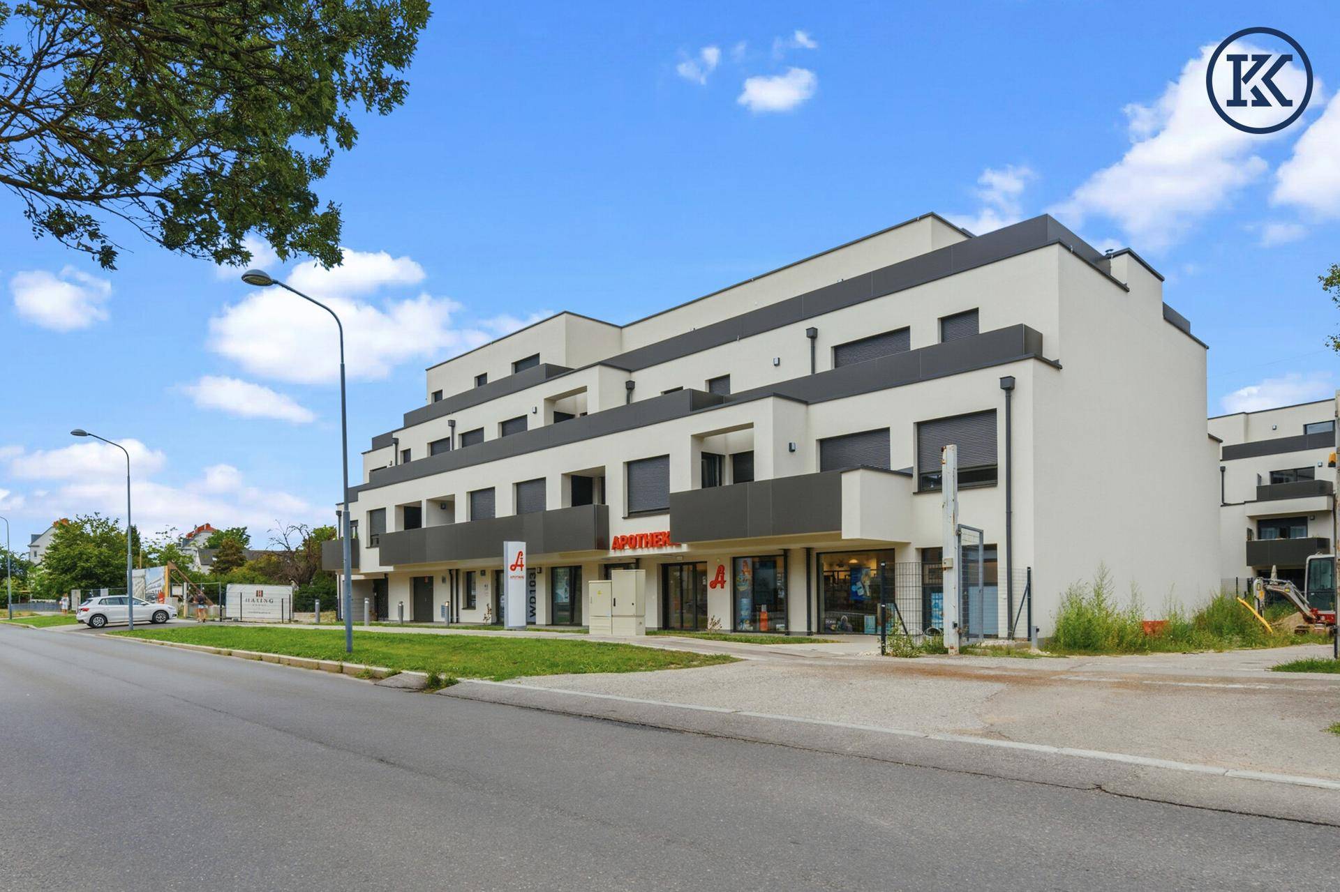 Ansicht des modernen Wohngebäudes mit Apotheke im Erdgeschoss und umliegender Straße.