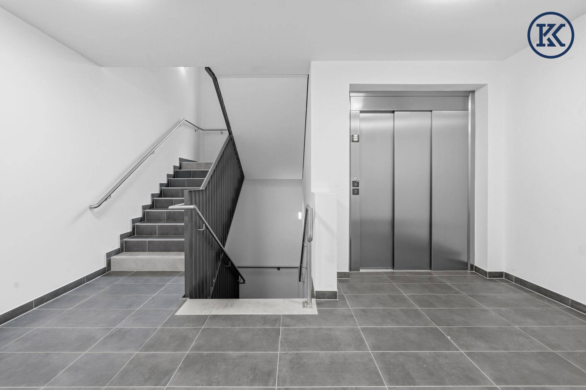 Heller Treppenaufgang mit modernem Geländer und einem Aufzug im Eingangsbereich des Gebäudes.