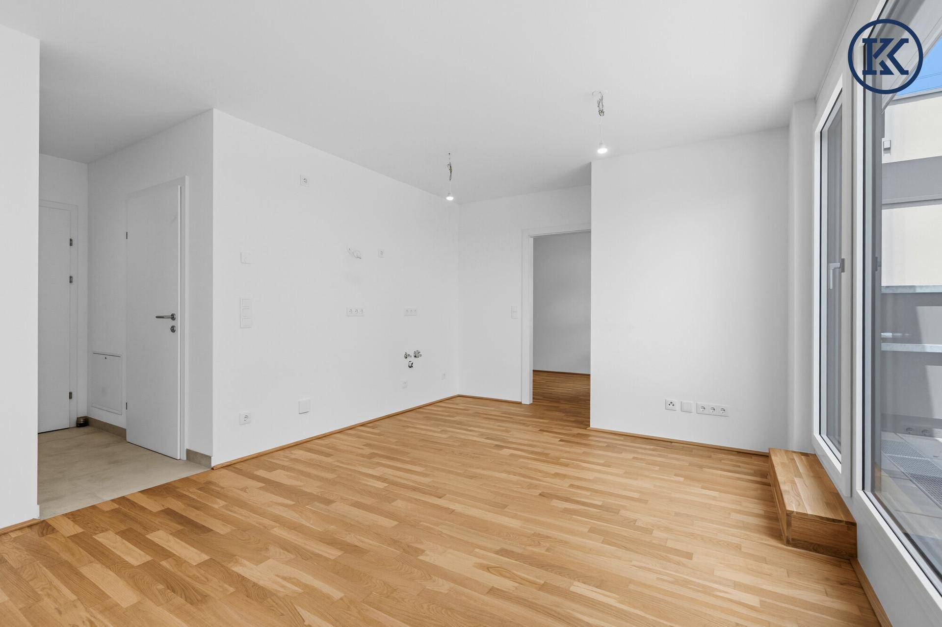 Geräumiges, leeres Wohnzimmer mit hellem Parkettboden und großen Fenstern für viel Tageslicht.