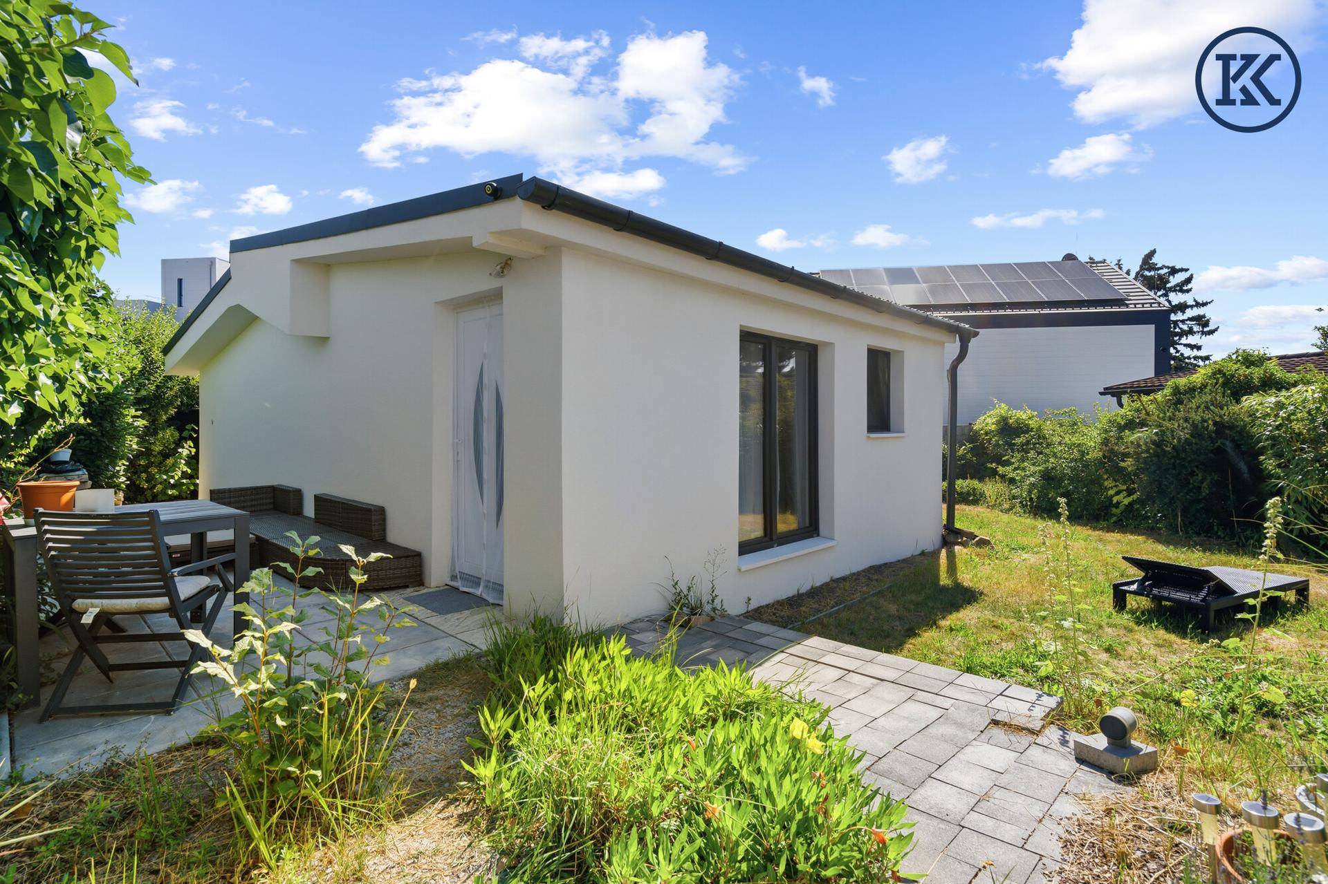 Gemütliche Terrasse am Haus mit Gartenmöbeln und einem gepflasterten Weg im Grünen.
