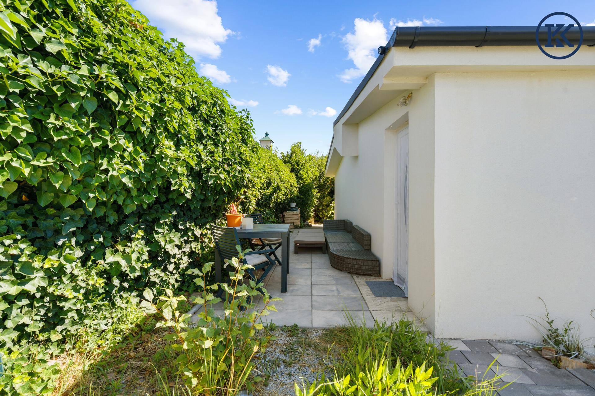 Sonnige Terrasse mit Gartenmöbeln, umgeben von einer hohen grünen Hecke für Privatsphäre.