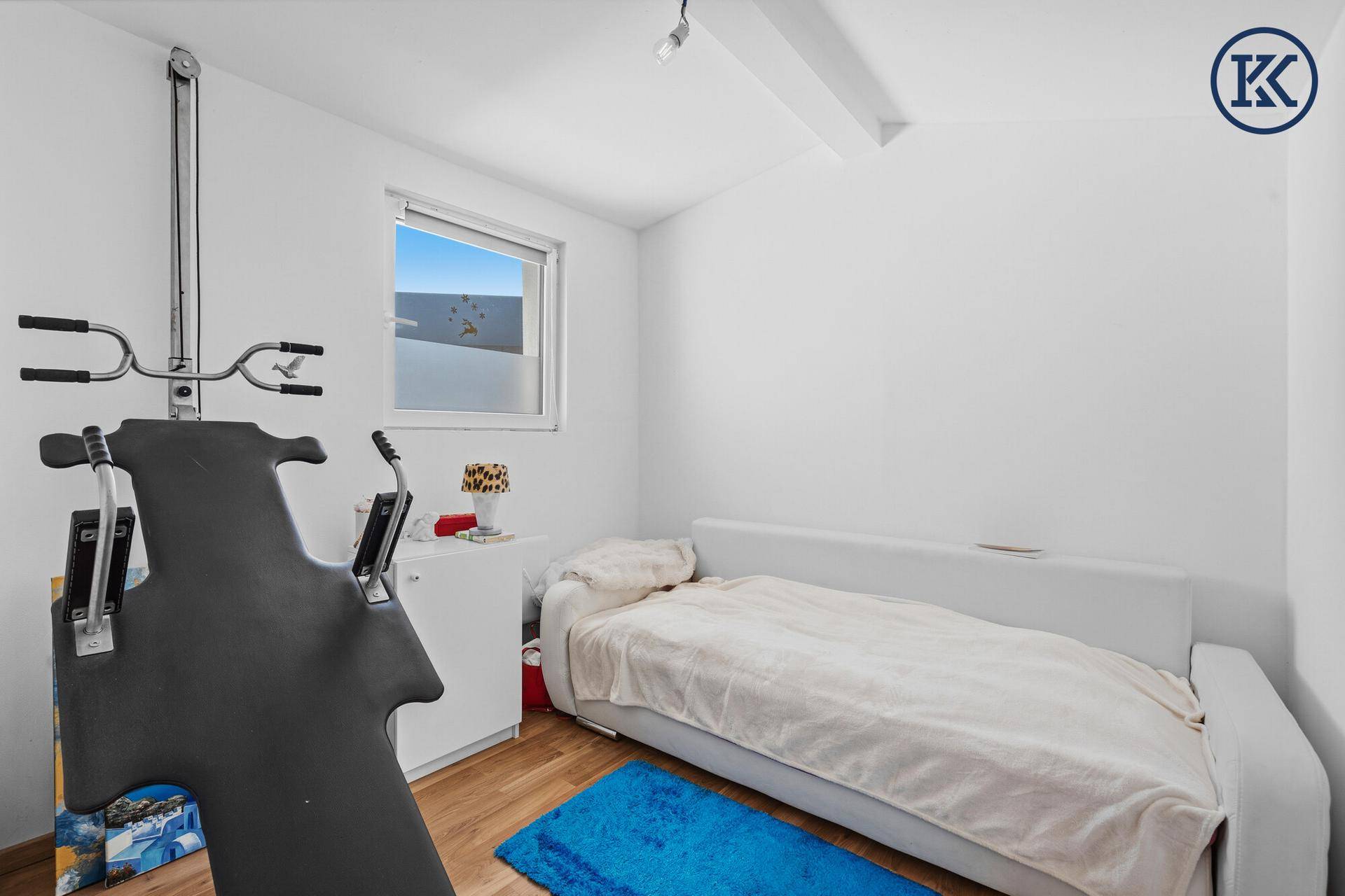 Schlichtes Schlafzimmer mit Einzelbett, Fenster und einem Fitnessgerät.