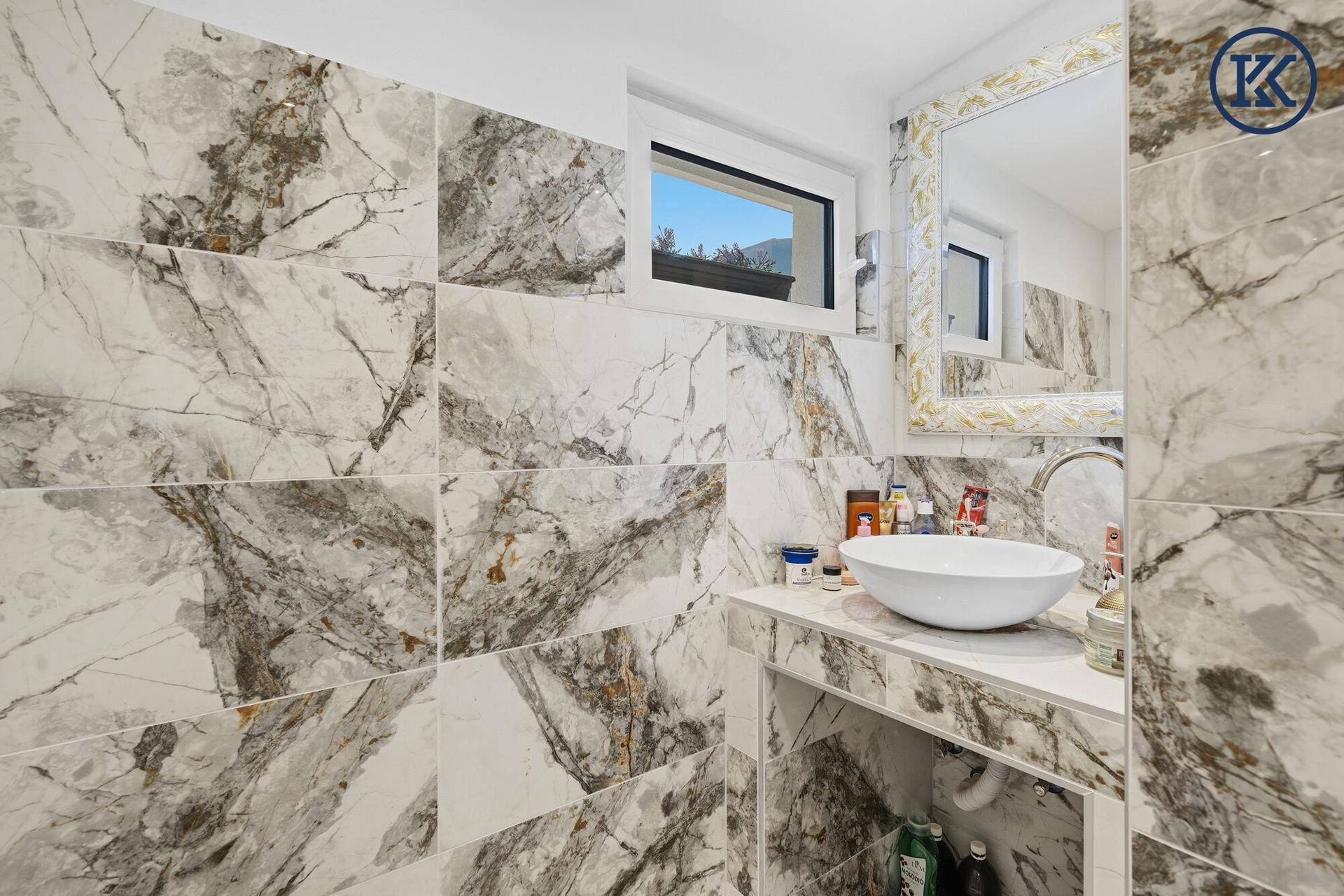 Elegantes Badezimmer mit Waschbecken, Marmorfliesen und einem Fenster für Tageslicht.