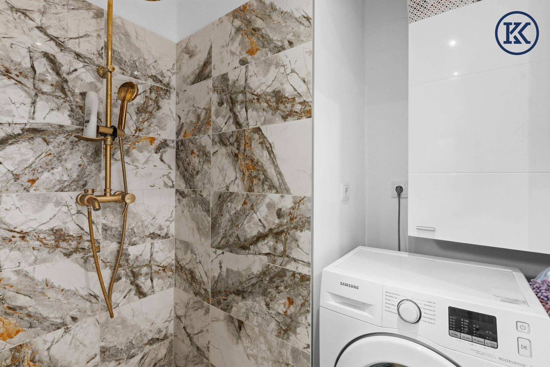Detaillierte Ansicht der Dusche mit goldenen Armaturen und der Waschmaschine im Badezimmer.