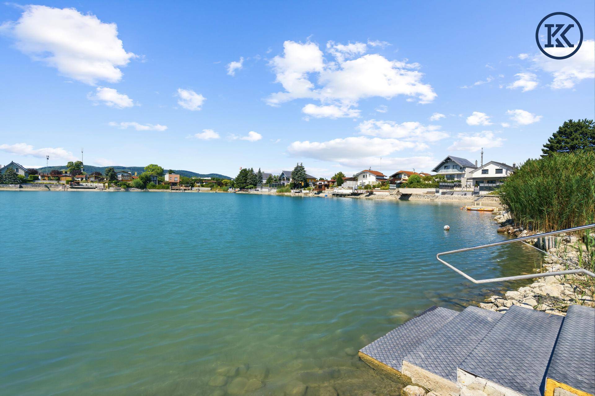 Blick auf den See mit Häusern am Ufer und klarem blauen Himmel an einem sonnigen Tag.