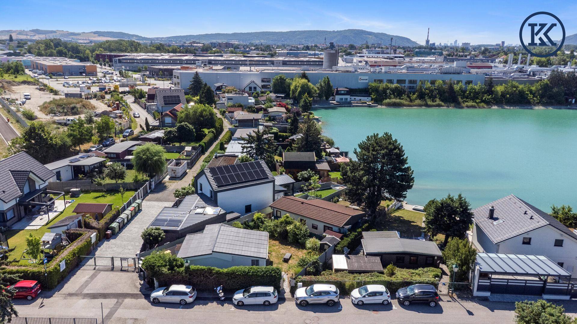 Luftaufnahme von Wohnhäusern, Parkplätzen und dem See im Hintergrund unter strahlendem Himmel.