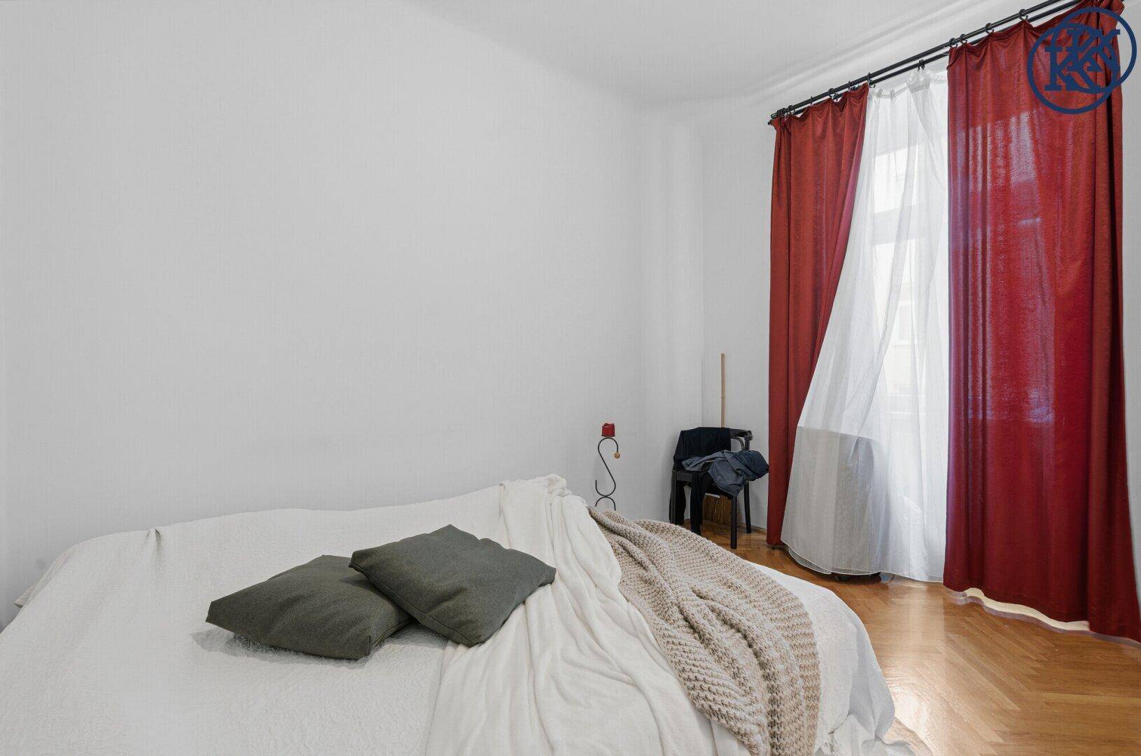 Helles Schlafzimmer mit Holzboden, weißem Bett und roten Vorhängen am Fenster.