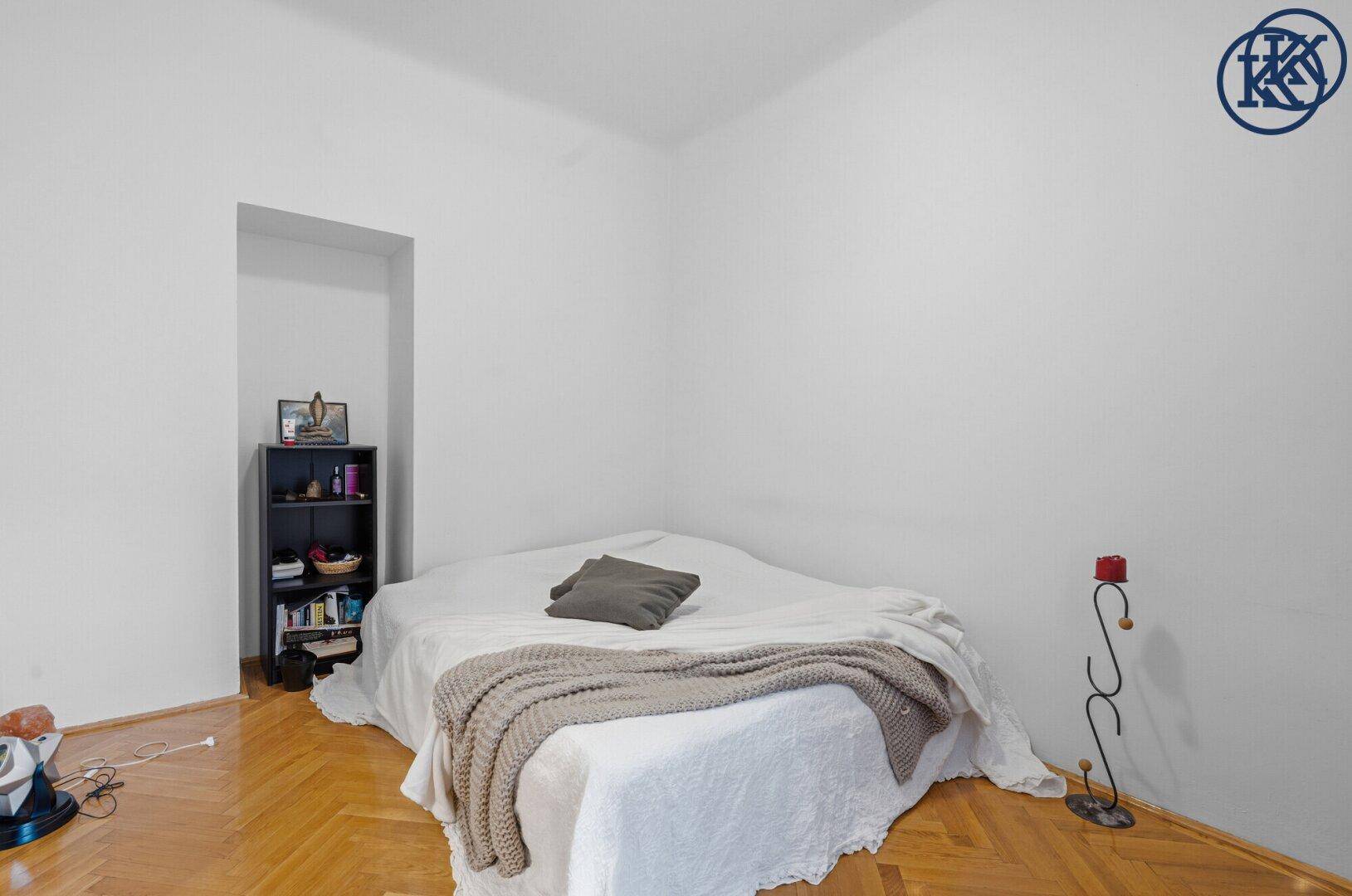 Schlafzimmer mit Holzboden, weißem Bett und einer Nische für ein kleines Regal.