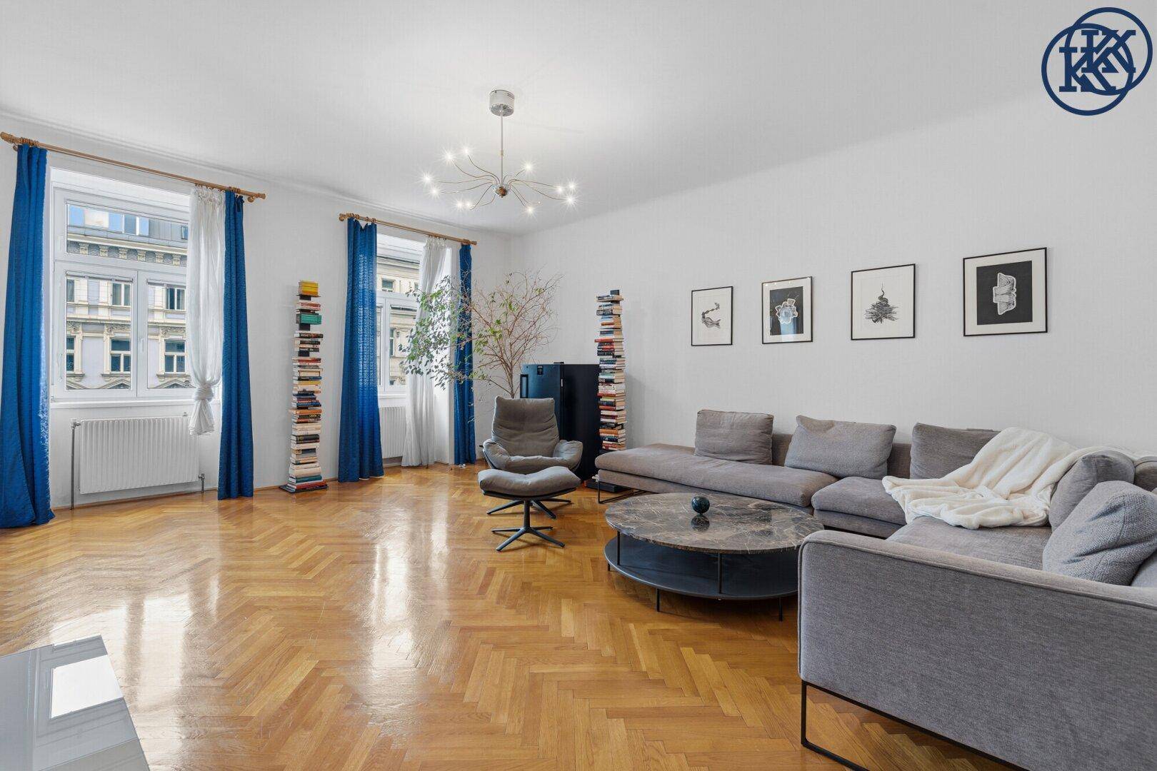 Geräumiges Wohnzimmer mit Fischgrätparkett, grauem Sofa und modernen Kunstwerken an der Wand.
