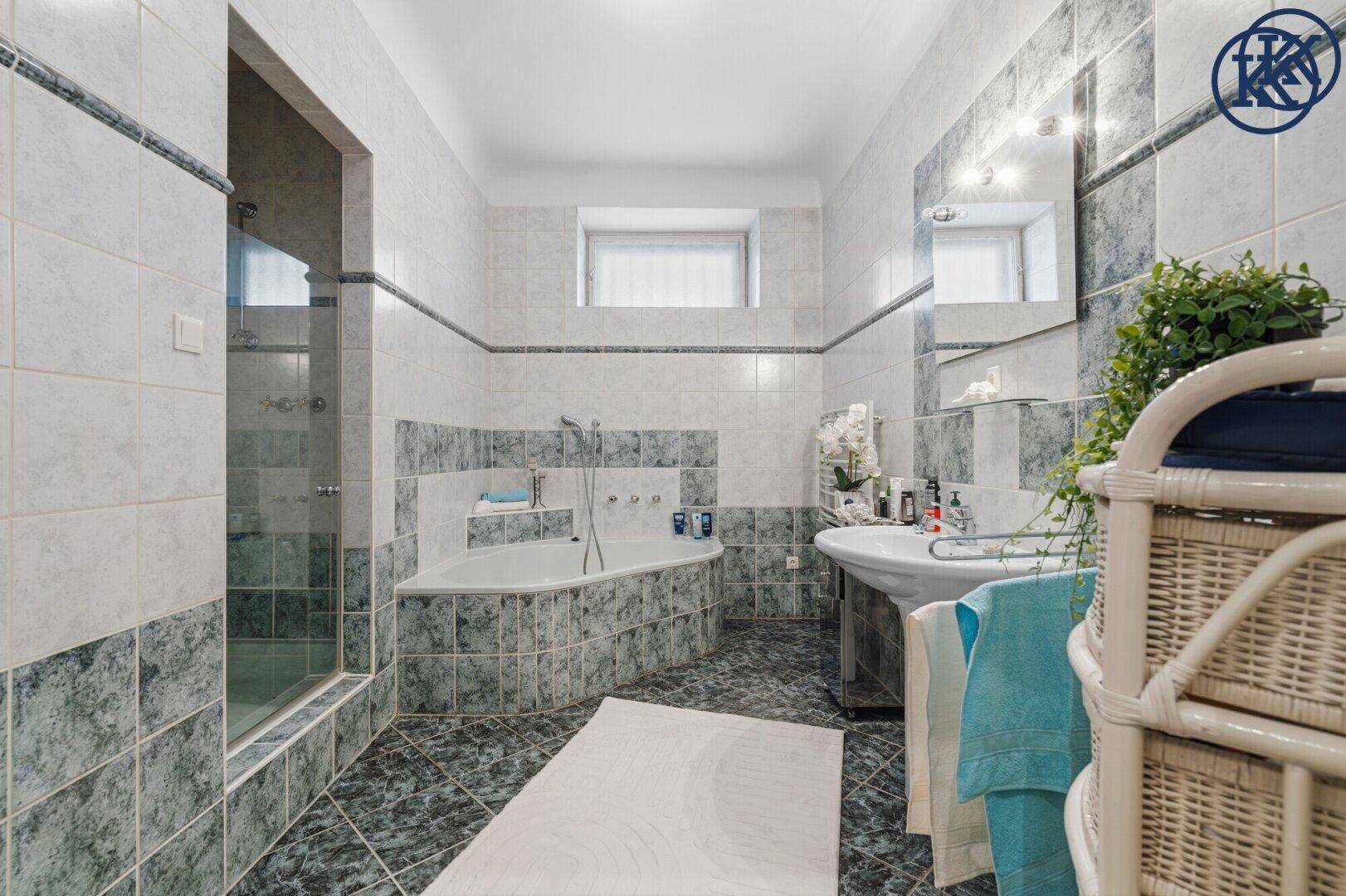 Geräumiges Badezimmer mit blaugrauen Fliesen, Badewanne und separater Dusche.