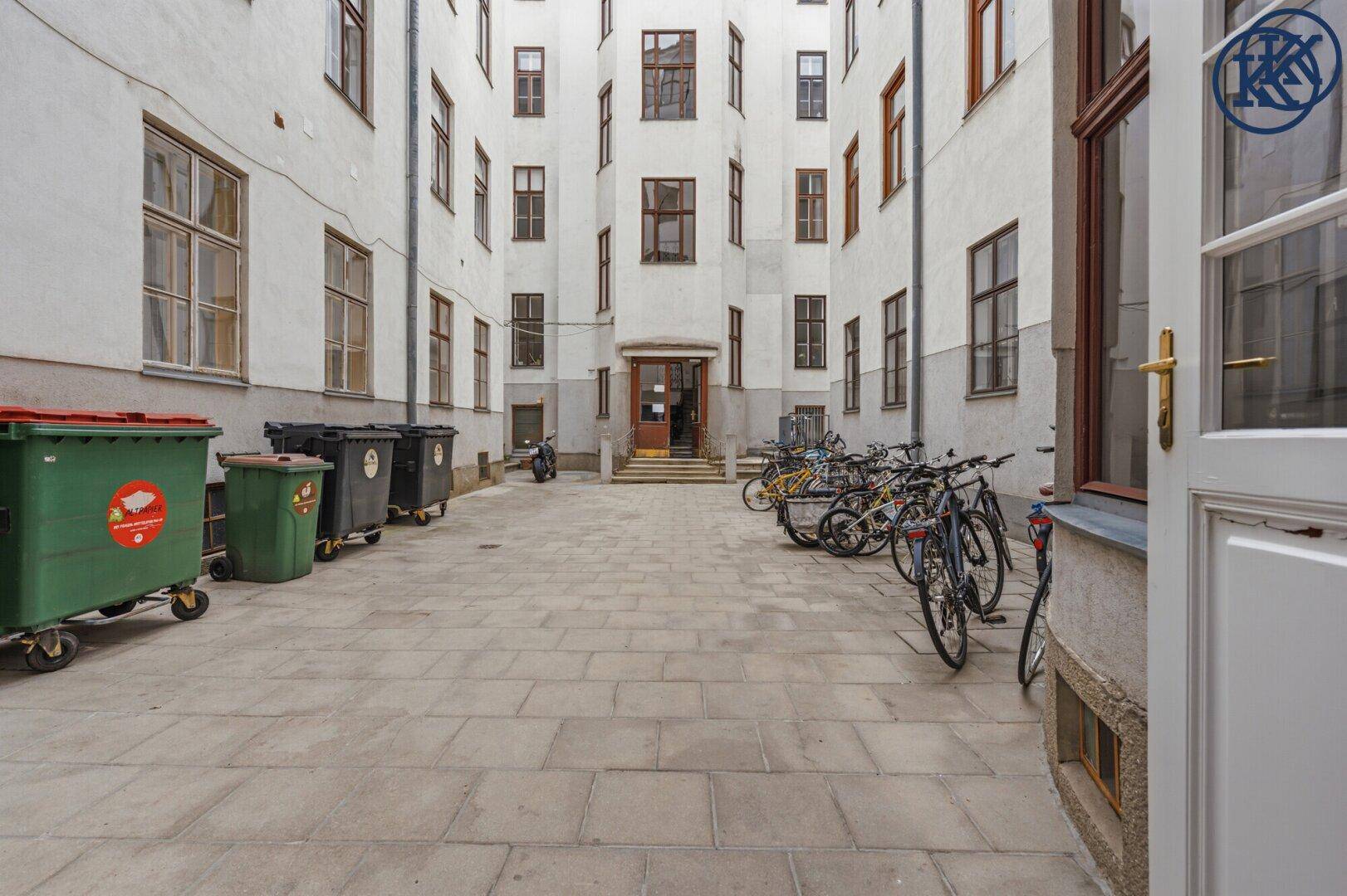 Innenhof mit Fahrradabstellplätzen, Mülltonnen und Fenstern der umliegenden Gebäude.