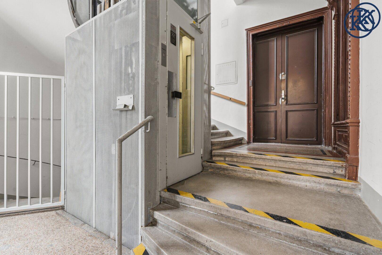 Moderner Aufzug in einem Treppenhaus mit Steinstufen und Handlauf.