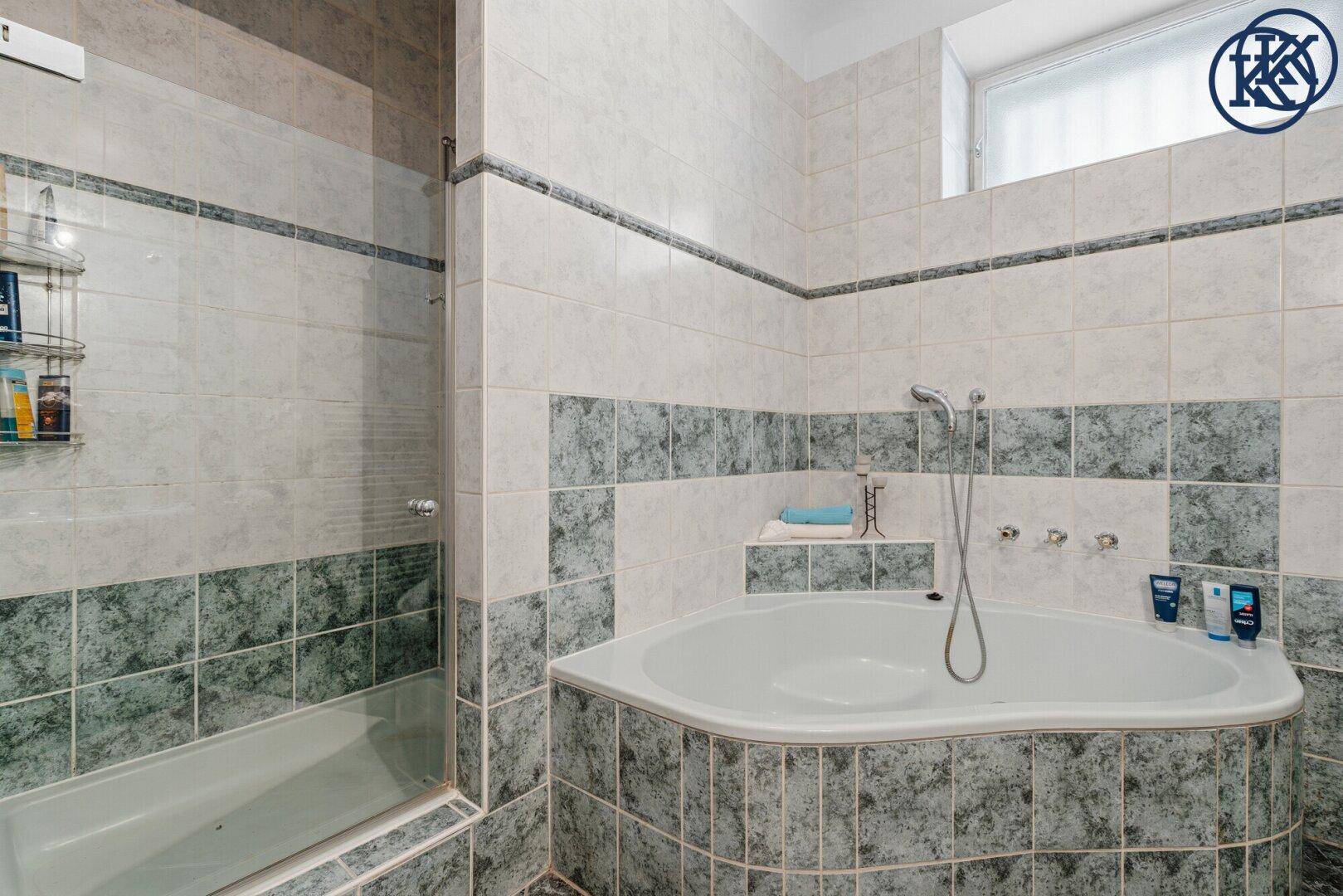Duschbereich und Badewanne mit blaugrauen Fliesen und integrierter Ablage.