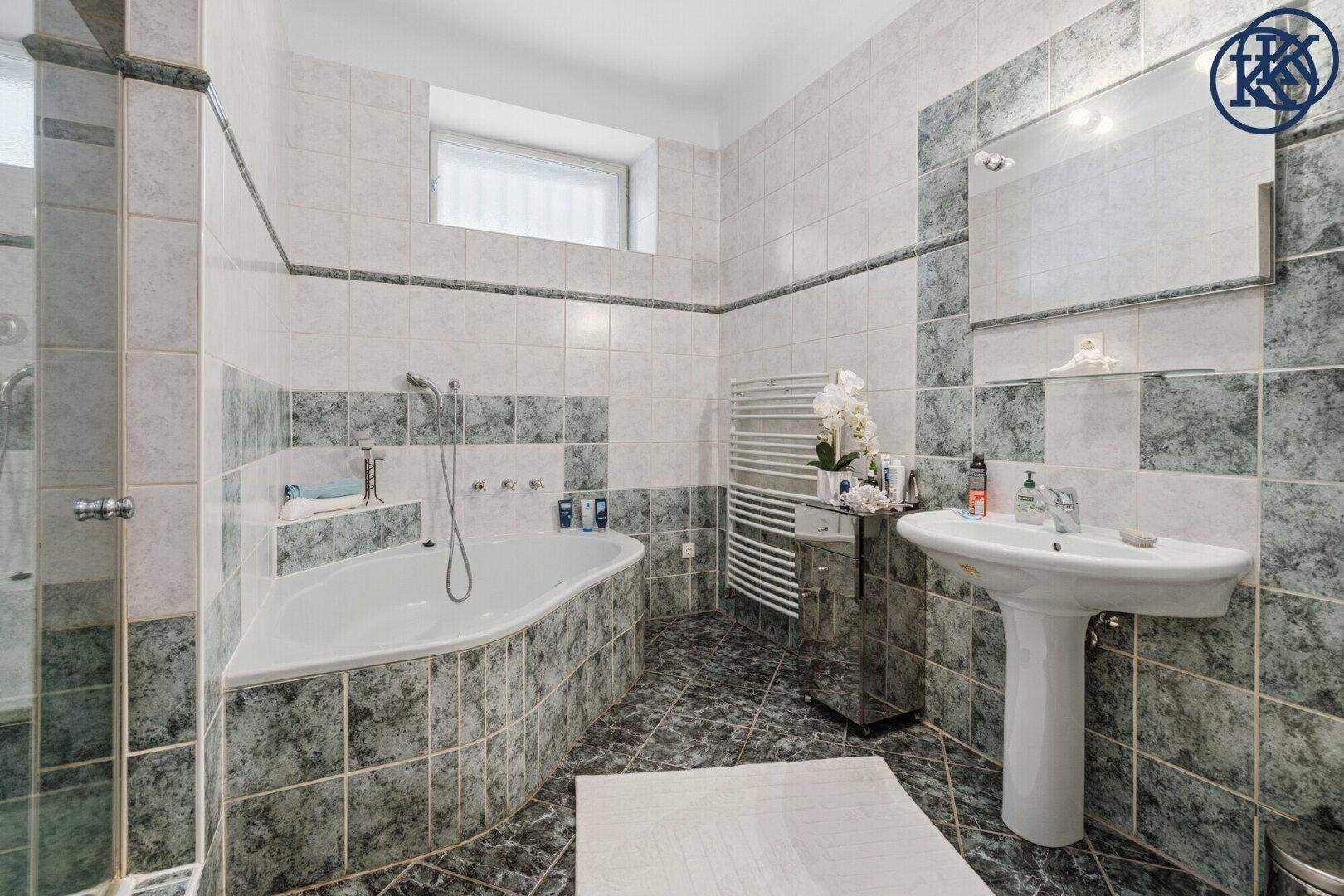 Badezimmer mit blaugrauen Fliesen, Badewanne, Waschbecken und beheiztem Handtuchhalter.