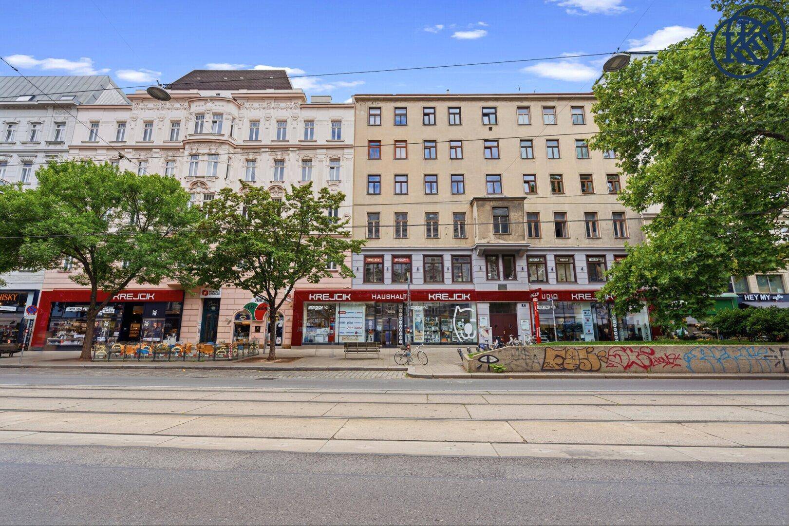 Straßenansicht eines Gebäudes mit Geschäften im Erdgeschoss und Straßenbahnschienen.