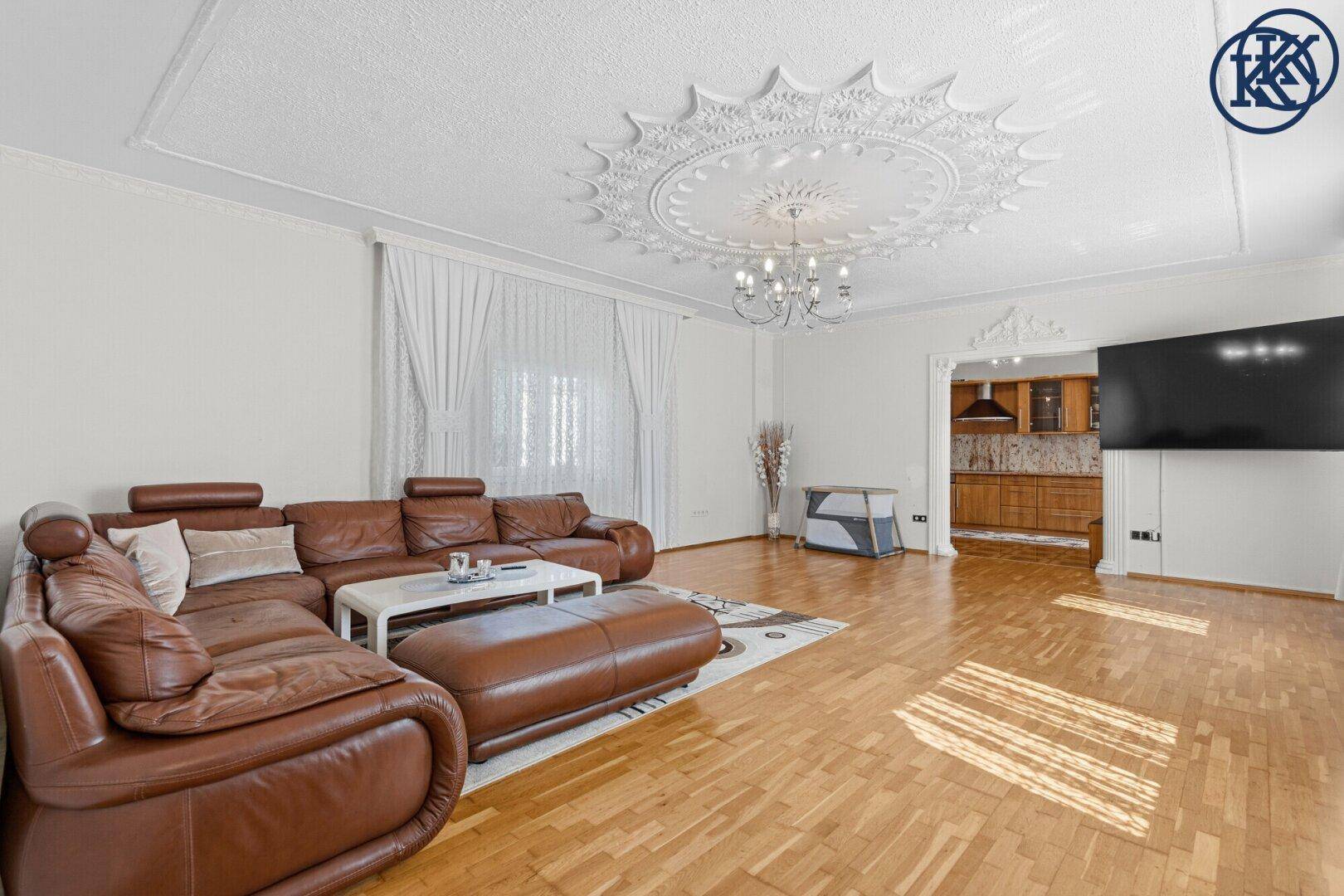 Gemütliches Wohnzimmer mit braunem Ledersofa, Parkettboden und dekorativer Stuckdecke.