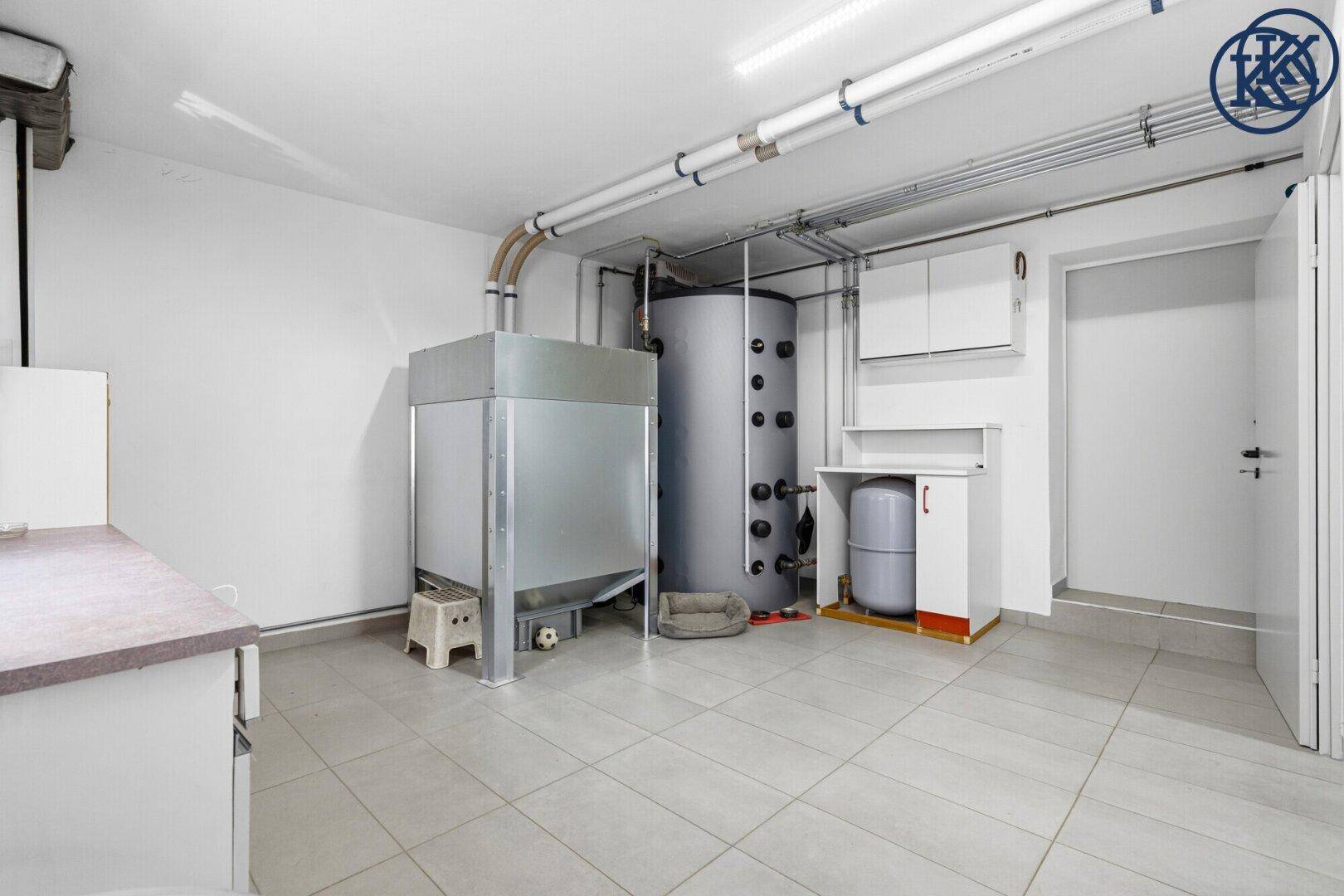 Geräumiger Heizungsraum im Keller mit großem Boiler und sichtbaren Rohrleitungen, funktional und hell.
