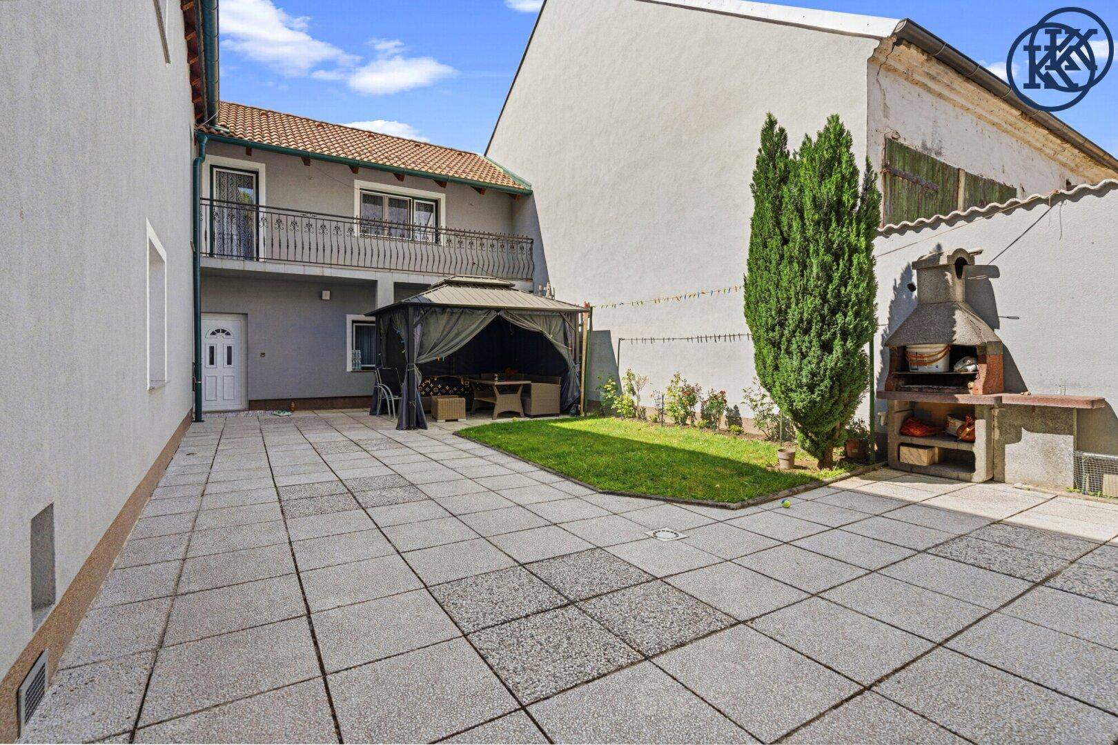 Große gepflasterte Terrasse mit Gartenlaube, Sitzgelegenheiten und Grillplatz, ideal für entspannte Stunden im Freien.