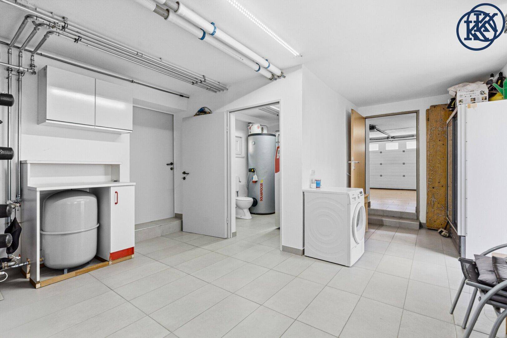 Funktionaler Hauswirtschaftsraum mit Waschmaschine und Zugang zur Garage, hell gefliest.