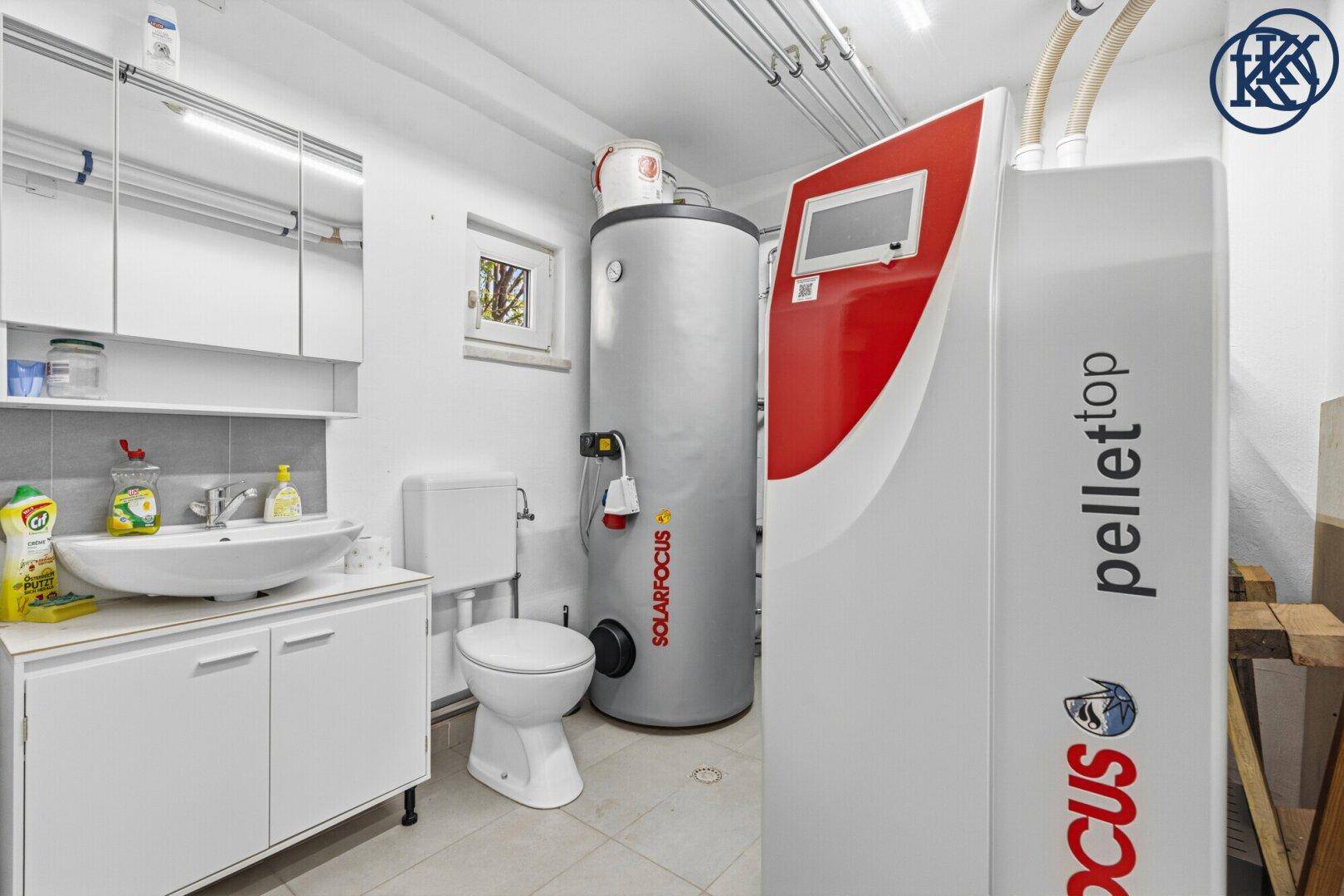 Heller Hauswirtschaftsraum mit Pelletheizung, Waschbecken, Toilette und Fenster im Untergeschoss.