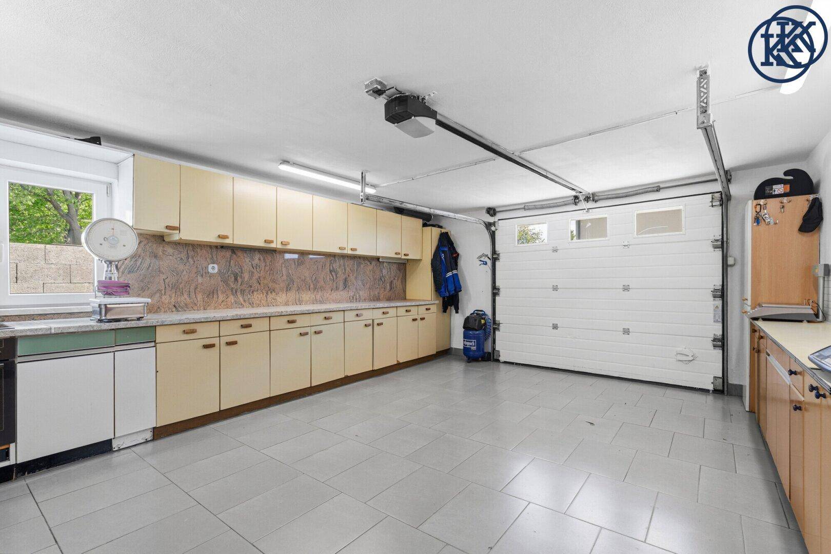 Geräumige Garage mit Rolltor, gefliestem Boden und praktischen Einbauschränken entlang der Wand.
