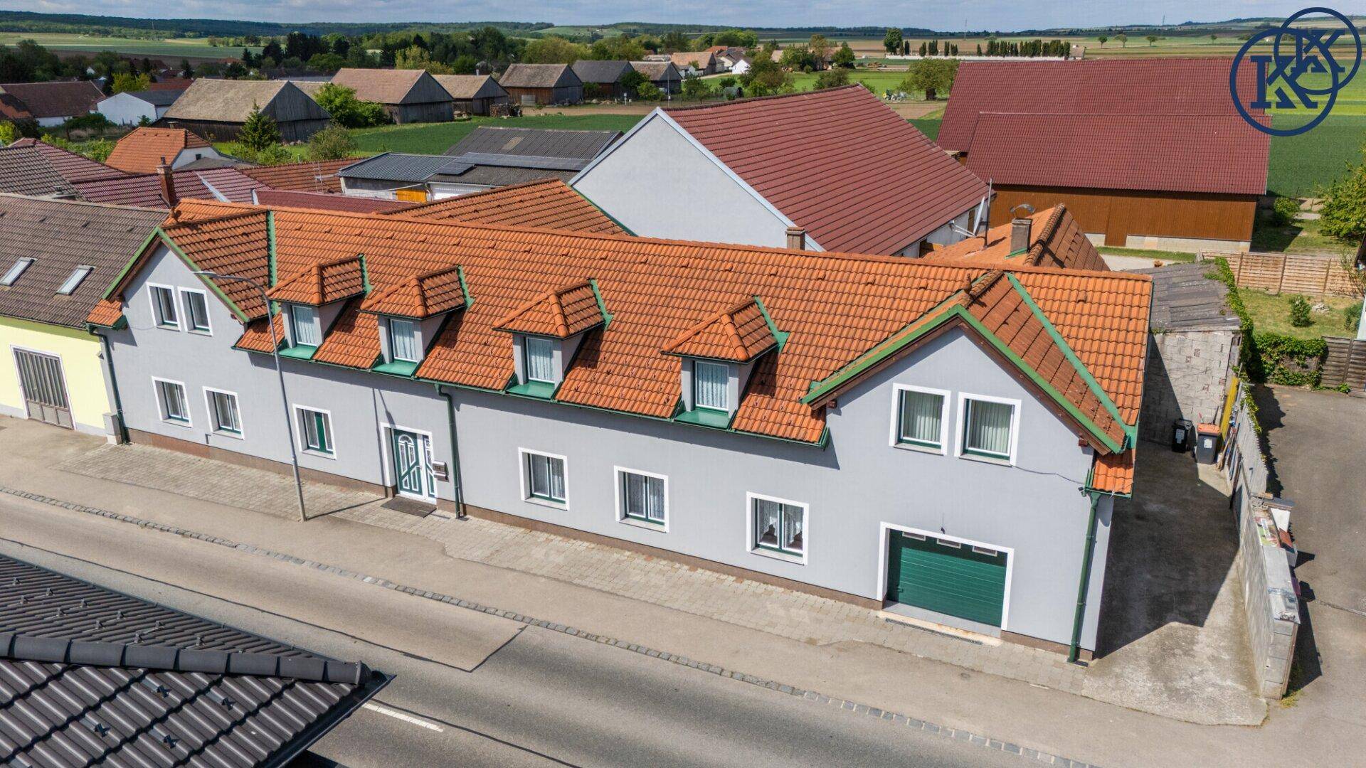 Vogelperspektive des Anwesens mit rotem Ziegeldach und ländlicher Umgebung unter blauem Himmel.