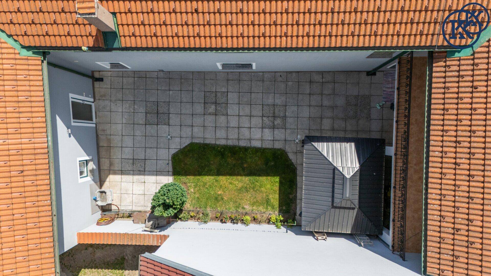 Draufsicht auf den Innenhof mit gepflasterter Fläche, Rasen und einer Gartenlaube.