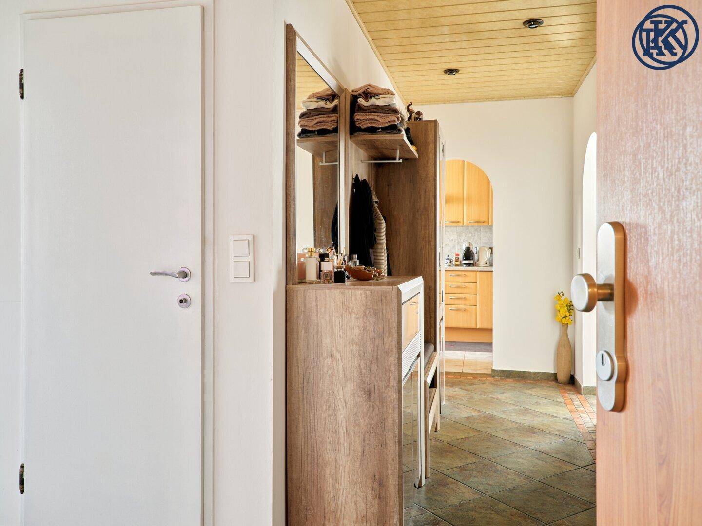 Eingangsbereich der Wohnung mit Garderobe, Spiegel und Blick in den Küchenbereich.