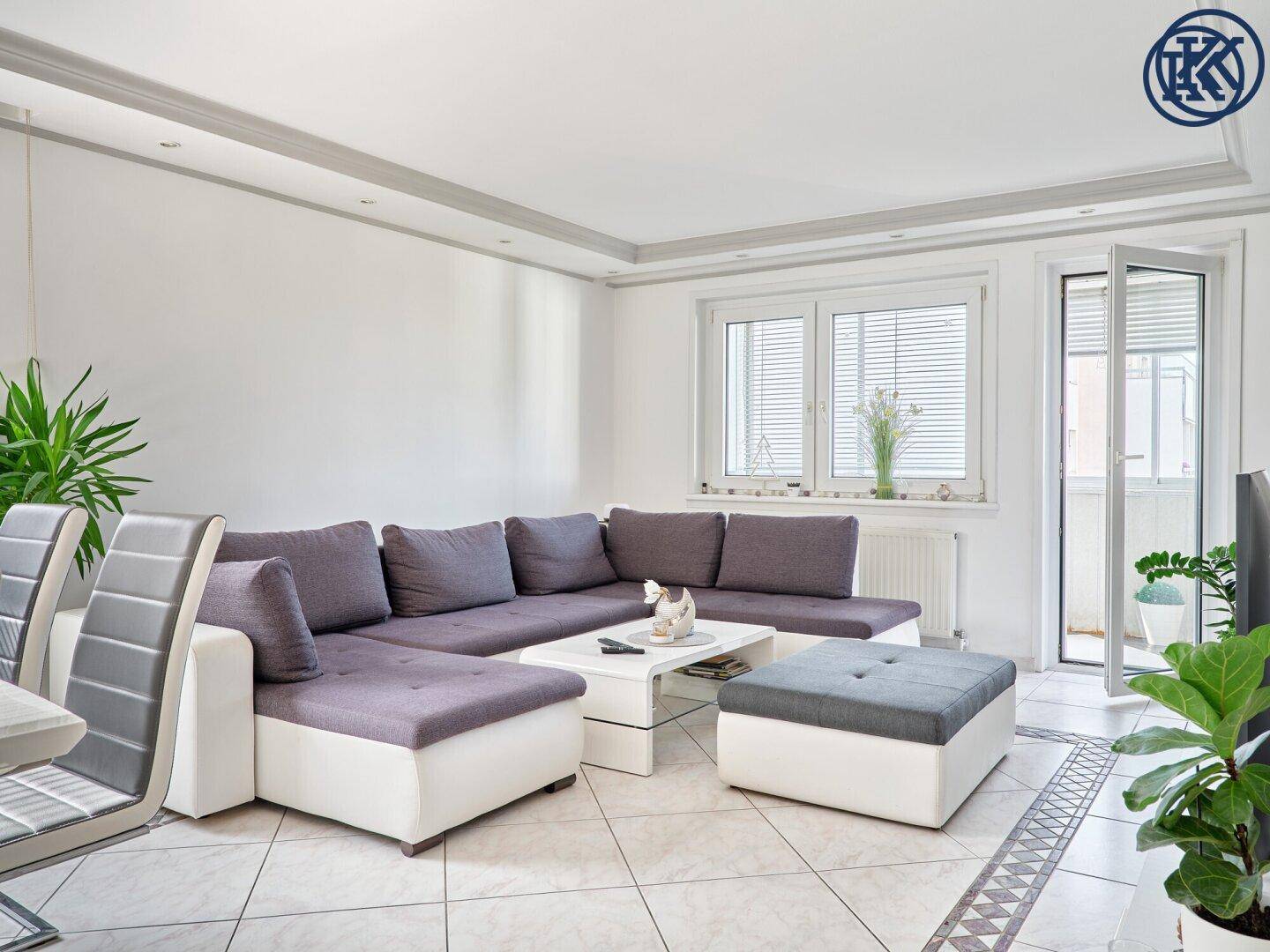 Heller Wohnbereich mit großem Ecksofa, Couchtisch und gefliestem Boden.
