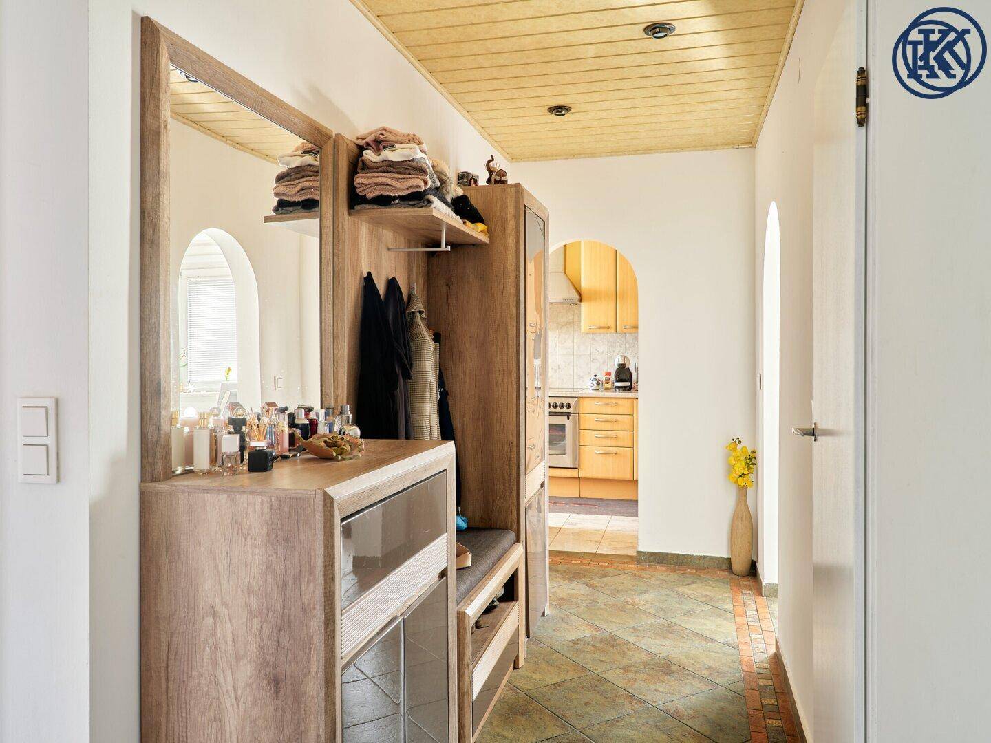 Heller Flur mit Holzdecke, gefliestem Boden und Garderobe, mit Blick in die Küche.