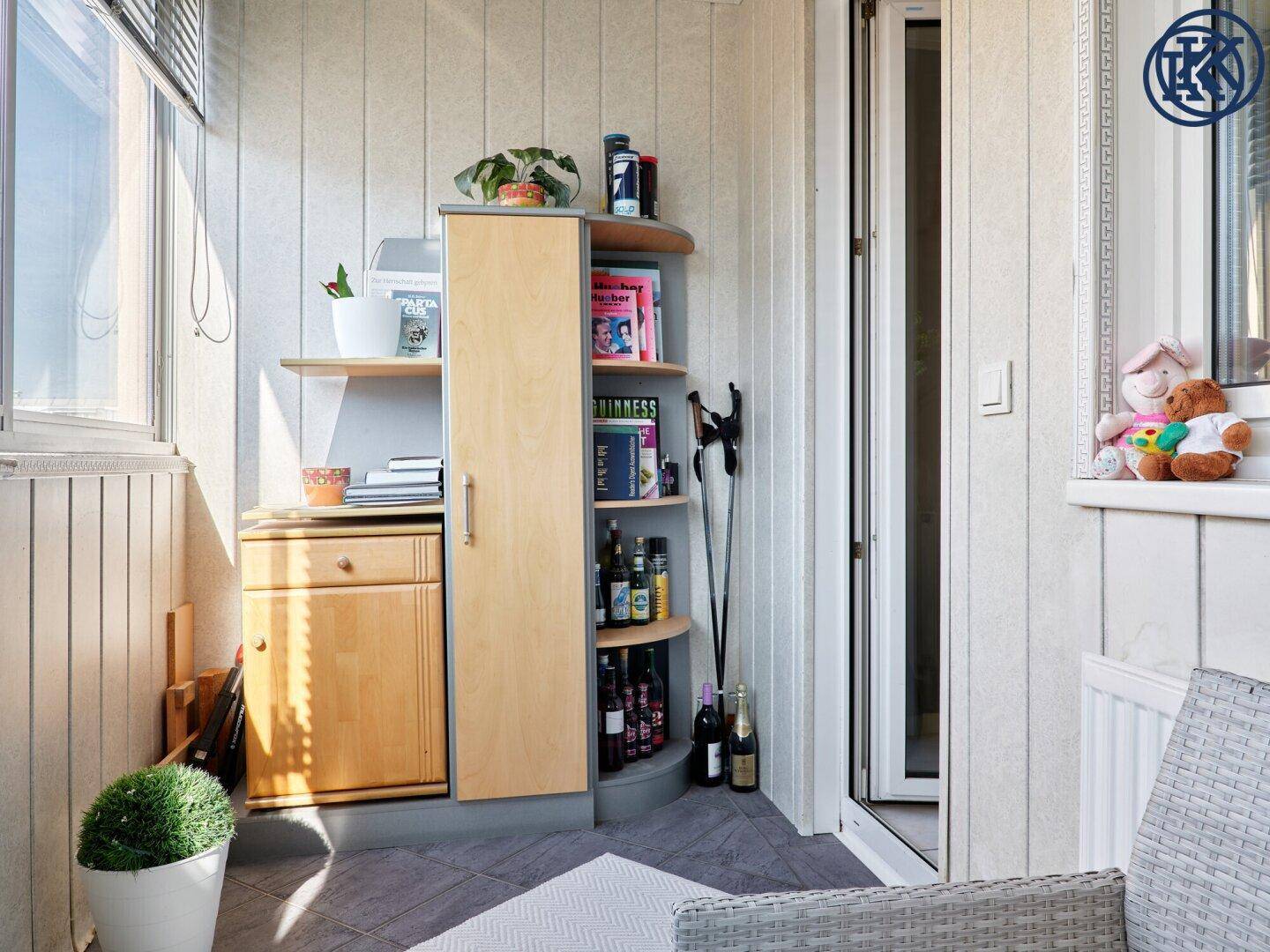 Verglaster Balkon mit kleinem Schrank, Regalen und seitlichem Fenster.
