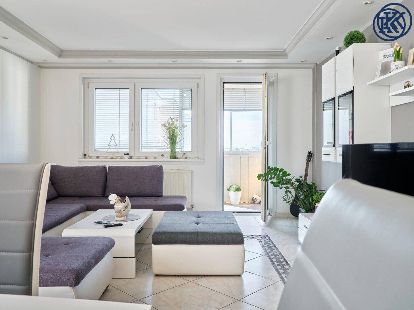 Heller Wohnbereich mit Sofa, TV-Möbel und Zugang zu einem kleinen Balkon.