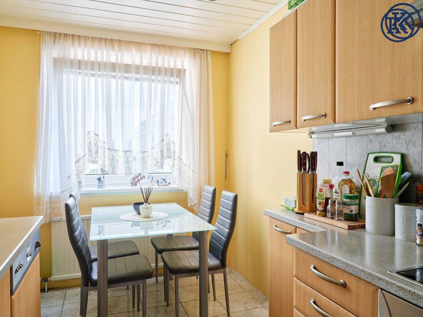 Helle Wohnküche mit Esstisch am Fenster und praktischen Holzschränken.