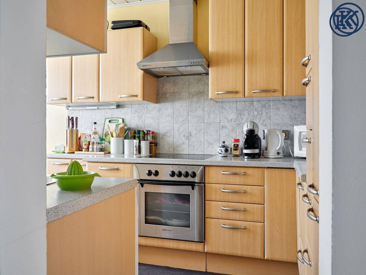 Funktionale Küche mit hellen Holzschränken, integriertem Backofen und Kochfeld.