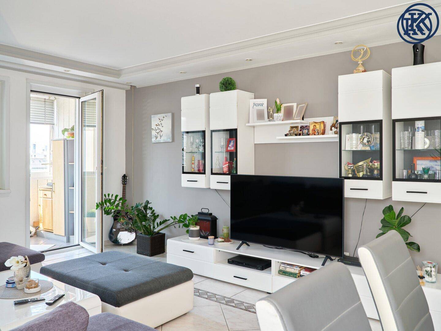 Wohnzimmer mit TV-Möbel, Sofa und Zugang zu einem kleinen Balkon.