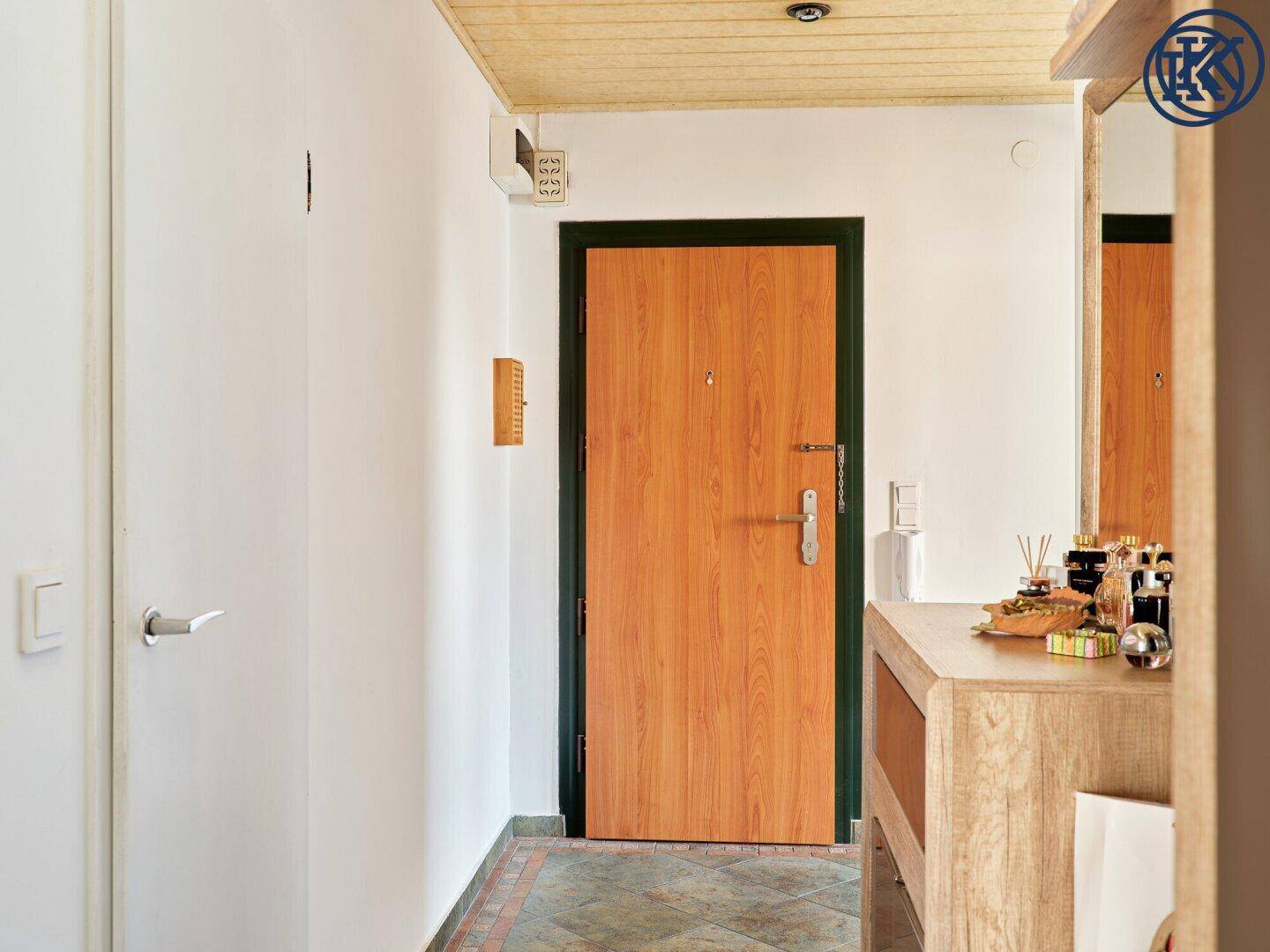Eingangsbereich der Wohnung mit Holztür, gefliestem Boden und einer Holzdecke.