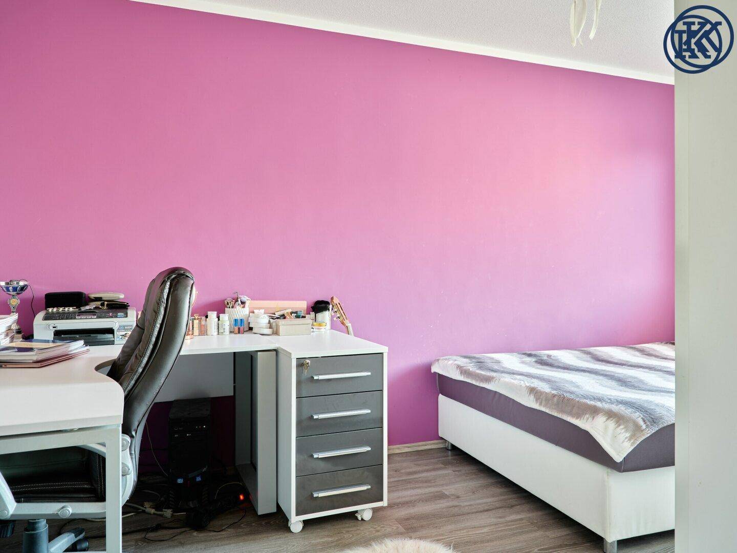 Schlafzimmer mit auffälliger violetter Wand, Schreibtisch und modernem Bett.