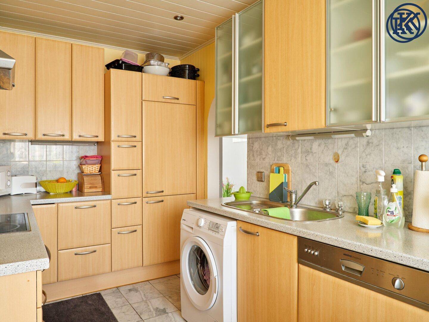 Praktische Küche mit Spülbecken, Geschirrspüler, Waschmaschine und Holzschränken.