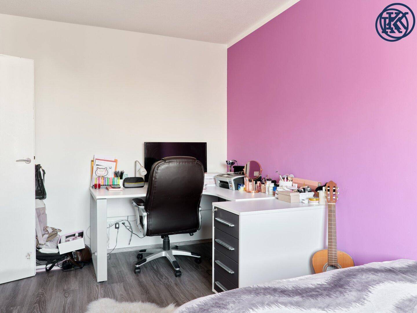 Helles Schlafzimmer mit Schreibtisch, Bürostuhl und violetter Akzentwand.