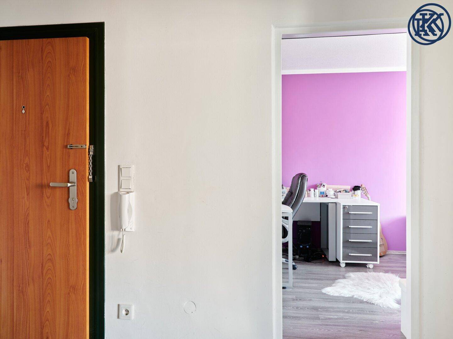 Heller Flur mit Holztür und Blick in ein Zimmer mit farbiger Wandgestaltung.