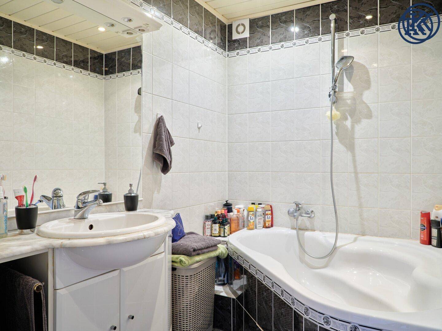 Badezimmer mit Waschbecken, großem Spiegel und Badewanne mit Duschfunktion.